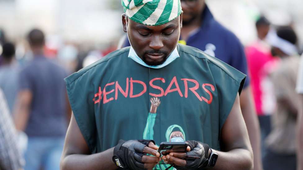 Un manifestante de #EndSars con una camiseta con el hashtag contra la brutalidad policial usando su teléfono celular en Lagos, Nigeria - octubre de 2020