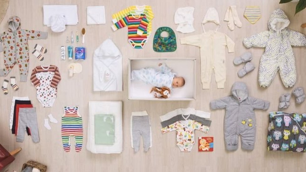 Bebé dentro de la caja de cartón junto a la ropa y otros objetos que son entregados a las madres en Finlandia (Foto: Kela)