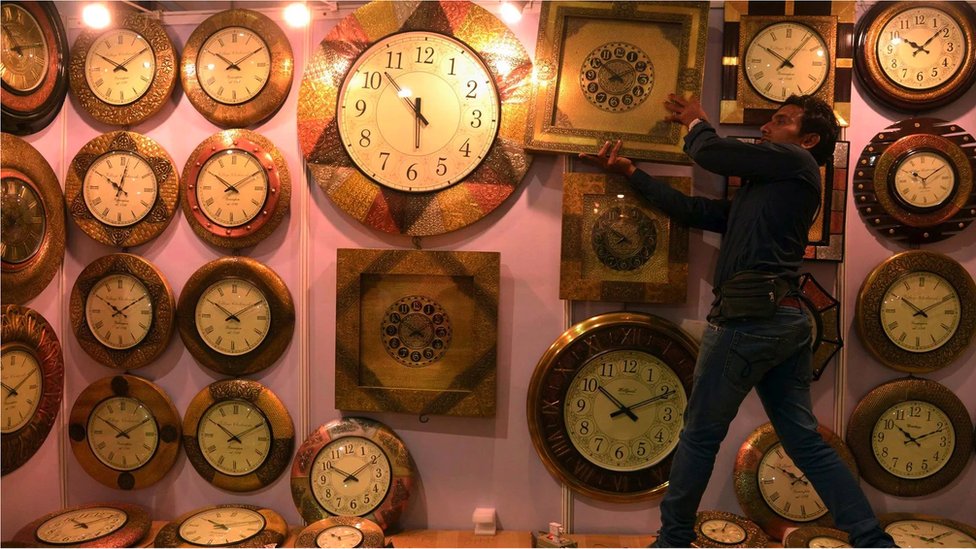 A wall full of clocks with a man grabbing one