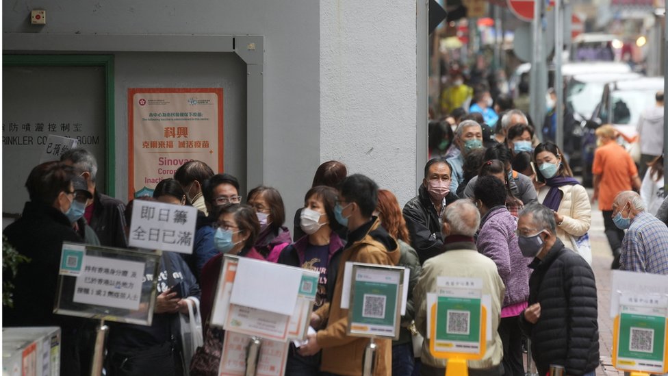 People wearing face masks queue outside a community vaccination centre to receive a dose of Sinovac Biotech"s CoronaVac COVID-19 vaccine, in Hong Kong, China February 10, 2022.