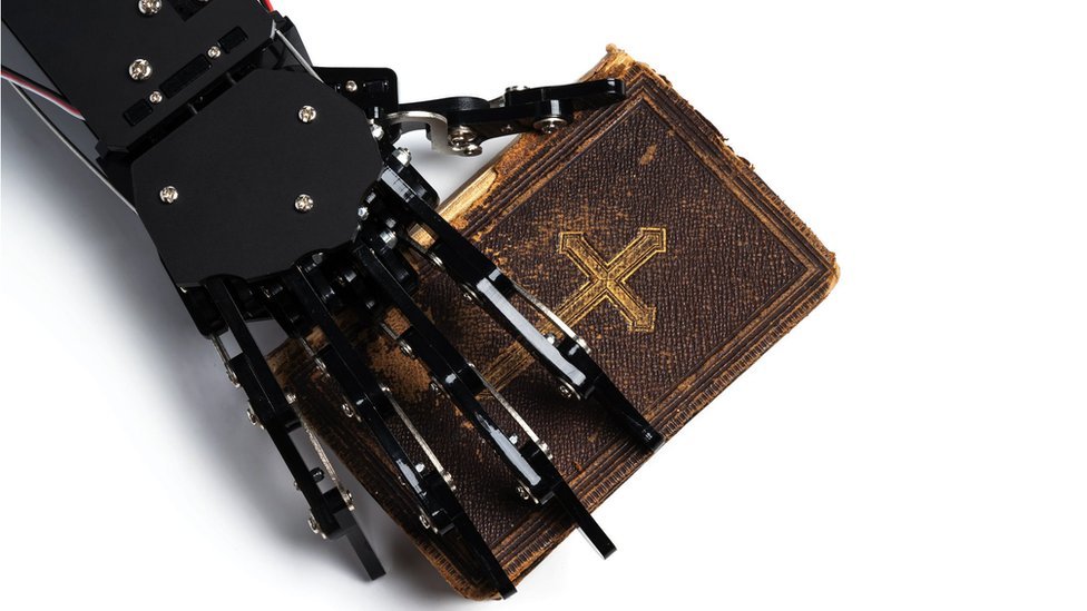 A robotic hand holds an old Bible