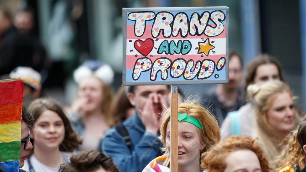 Участник держит табличку с надписью «Trans and Proud» во время марша Прайд в Глазго