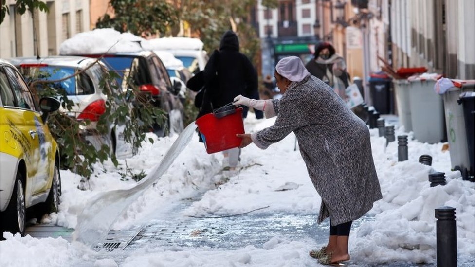 A woman throws water on a snow-covered street, following heavy snowfall, in Madrid, Spain January 11, 2021