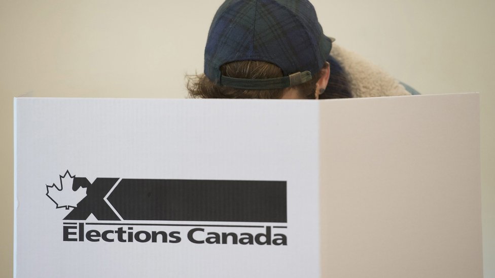 Избиратель опускает бюллетень за табличкой "Выборы в Канаде".