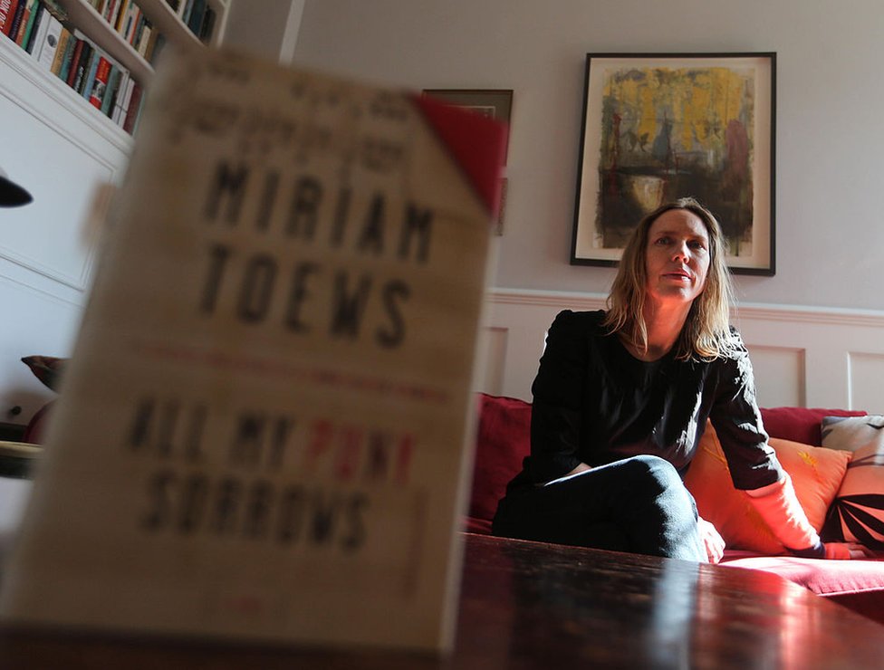 La portada de &quot;All My Punny Sorrows&quot; en primer plano y detrás su autora Miriam Toews, en su casa de Toronto, Ontario, Canadá, el 8 de abril de 2014.