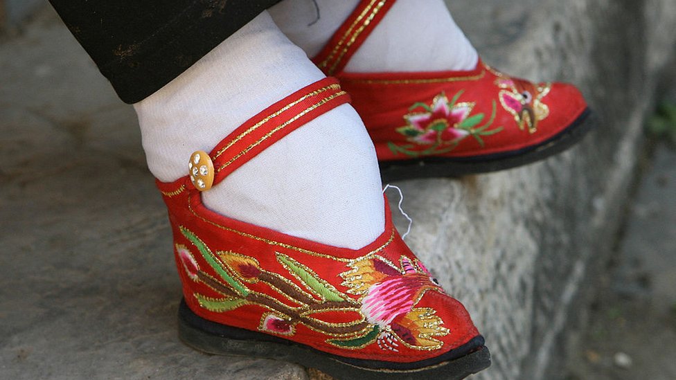 Dentro de unos zapatos muy pequeños, en rojo y con bordados delicados, están los pequeños de una mujer adulta que fue vendada desde niña.