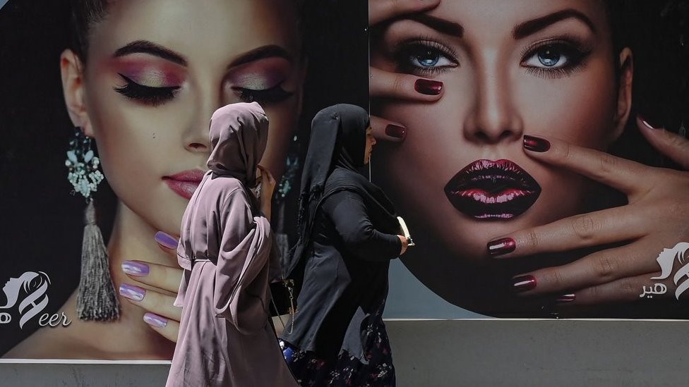Mujeres caminan frente a un anuncio publicitario con modelos en Kabul
