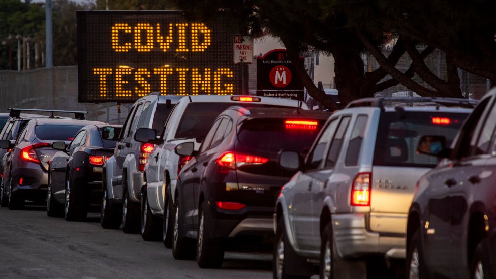 Длинная очередь автомобилей для прохождения тестов на Covid-19 в сумерках на стадионе Long Beach City College-Veterans Memorial Stadium в декабре