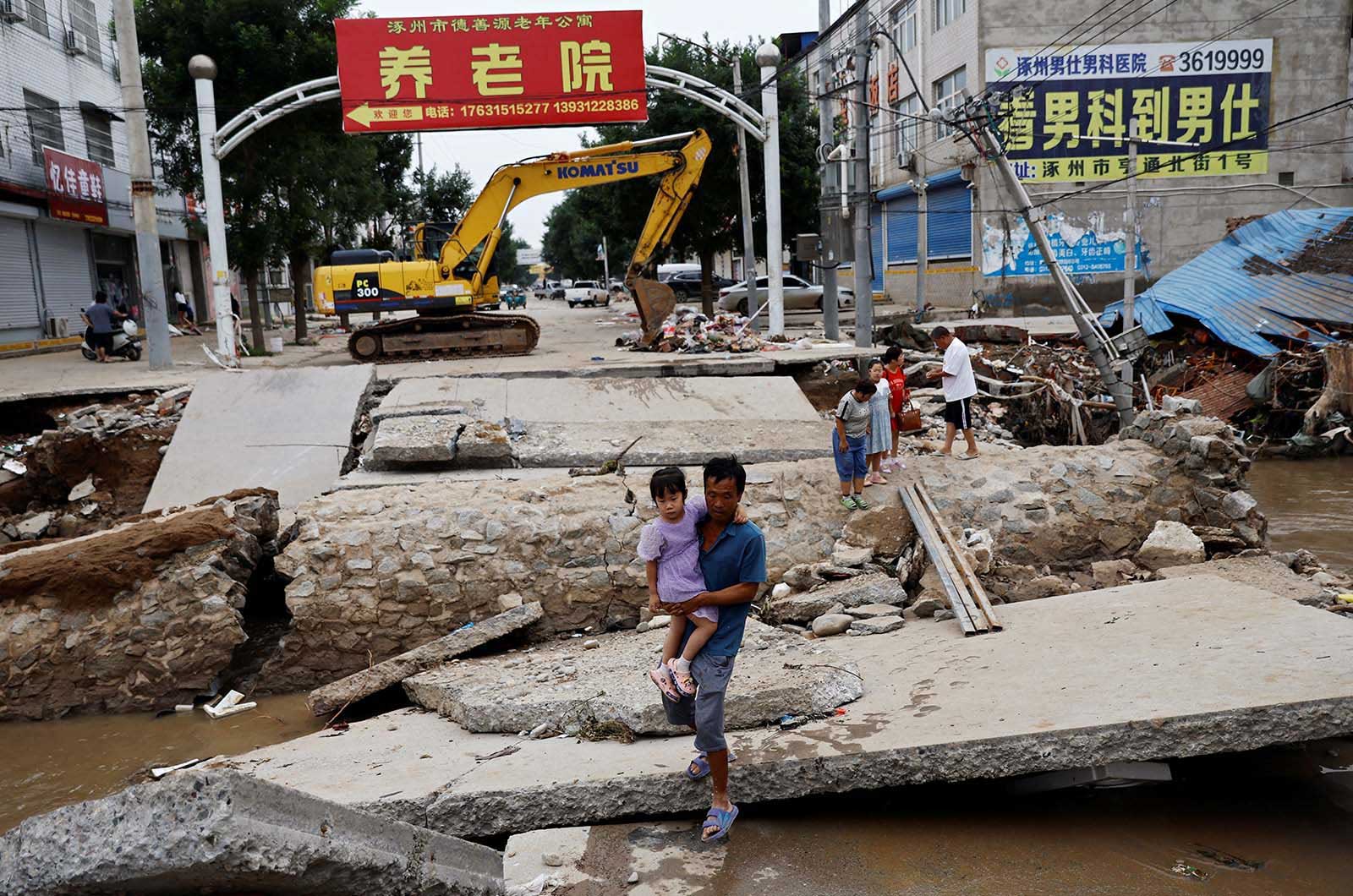 A man in Zhuozhou, Hebei province, China, holds a child as he walks across a damaged bridge after Typhoon Doksuri - 7 August, 2023