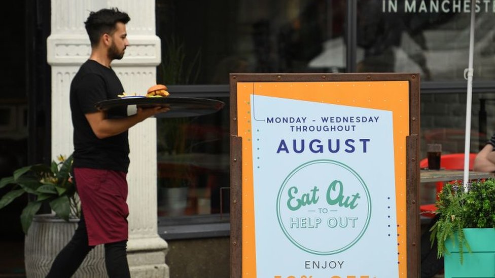 Waiter walking past an ''eat out to help out'' sign