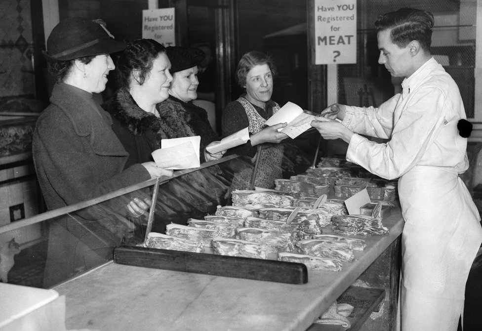 A shop assistant in a butcher's shop in south London cuts a coupon out of a customer's ration book on the first day of rationing in Britain