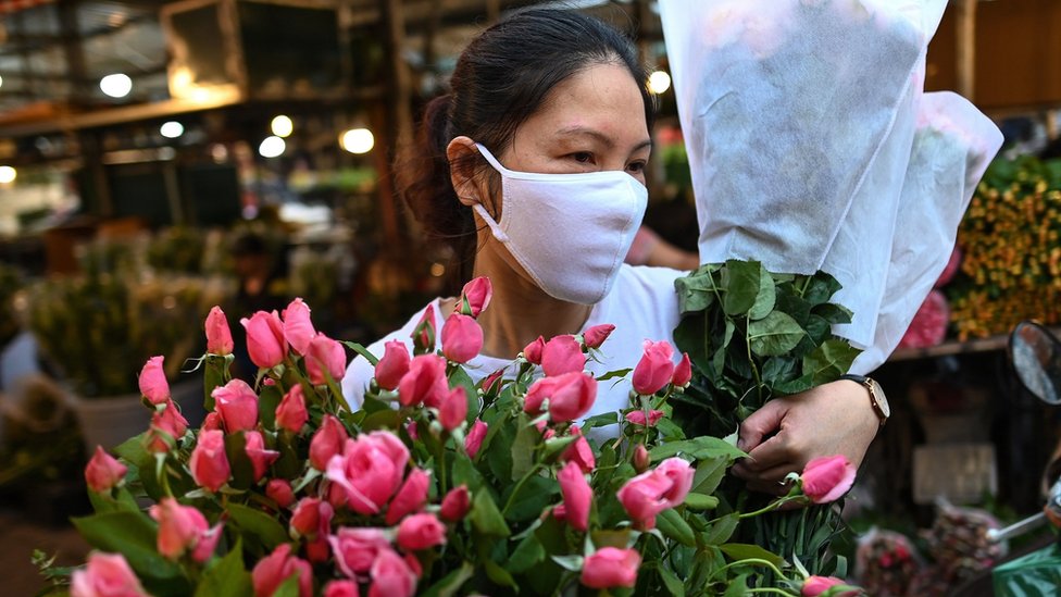Женщина в маске несет цветы в Ханое