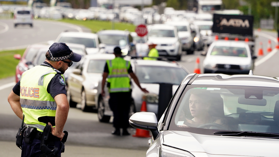 Police checking the border entry requirements of car passengers waiting to cross into Queensland from New South Wales