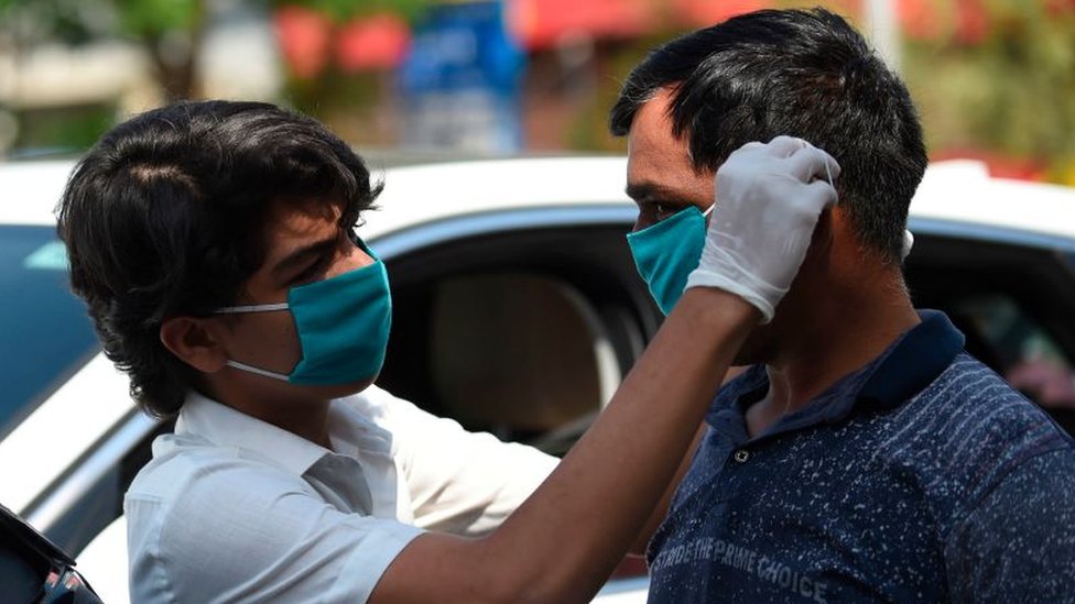 Un voluntario en India ayuda a un hombre con una mascarilla.