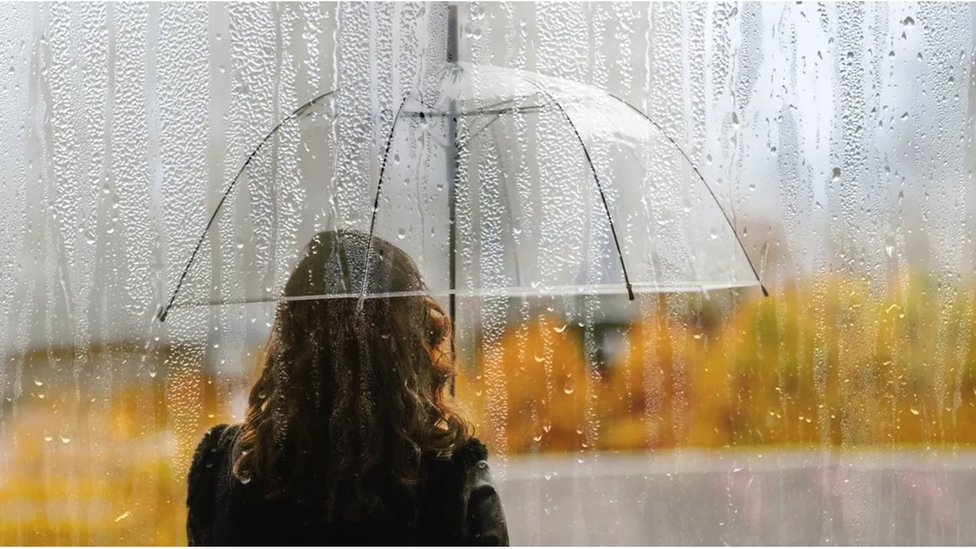 A woman holding an umbrella looks out at the rain