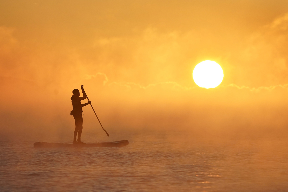 A paddle boarder silhouetted in the sea mist as the sun rises over Avon Beach in Dorset, England, 8 December 2022