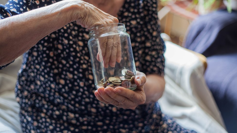 Adulta mayor introduce una mano en un frasco con monedas