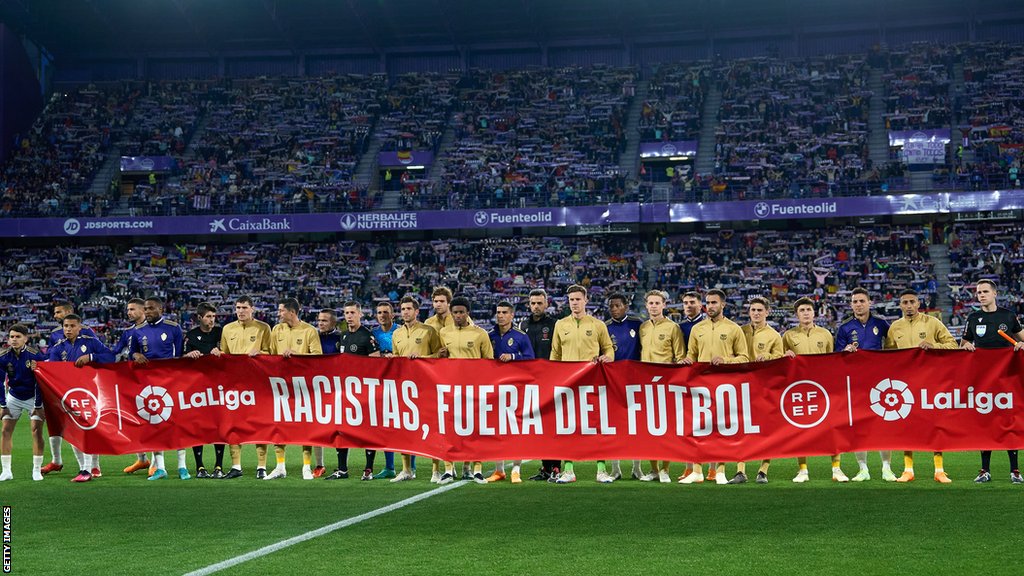 Los jugadores del Real Valladolid el Barcelona sostienen un cartel que lee: "Racistas fuera del fútbol"