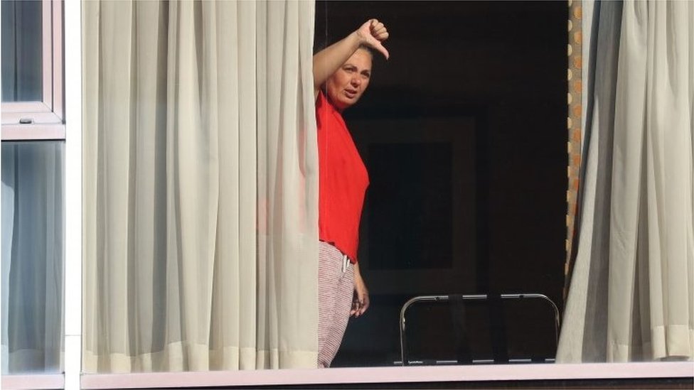 Uma mulher faz um gesto de polegar para baixo para jornalistas da janela do Radisson Blu Edwardian Hotel, perto do Aeroporto de Heathrow