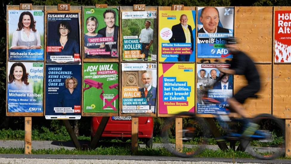 Велосипедист проезжает мимо нескольких плакатов предвыборной кампании в Бад-Фейльнбахе, Германия, 6 октября 2018 г.