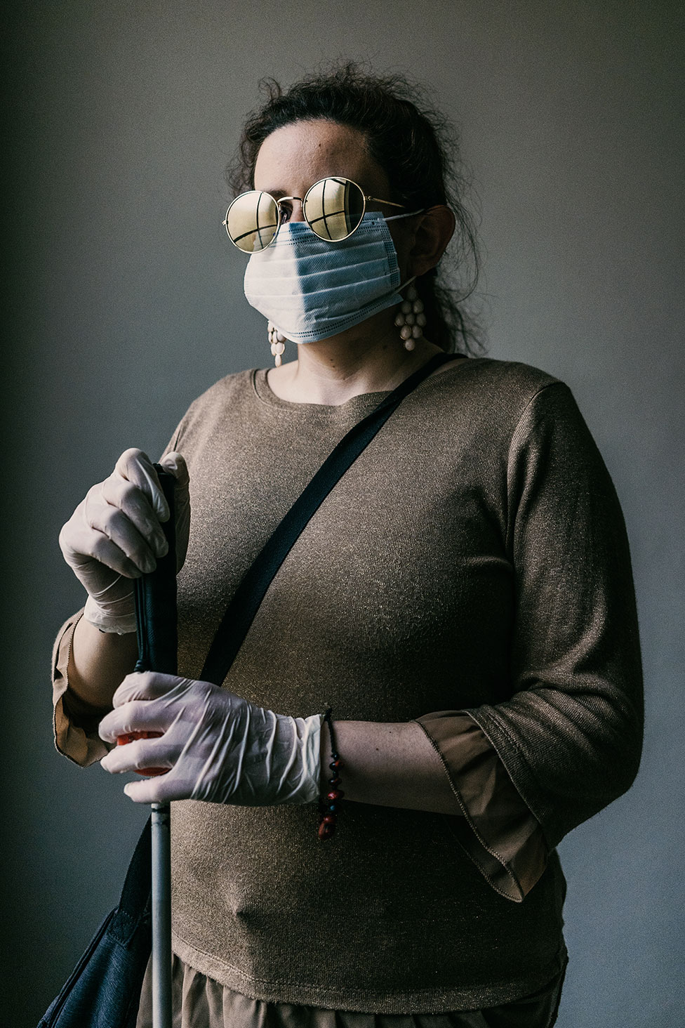 Слепая женщина стоит со своей тростью в маске и перчатках