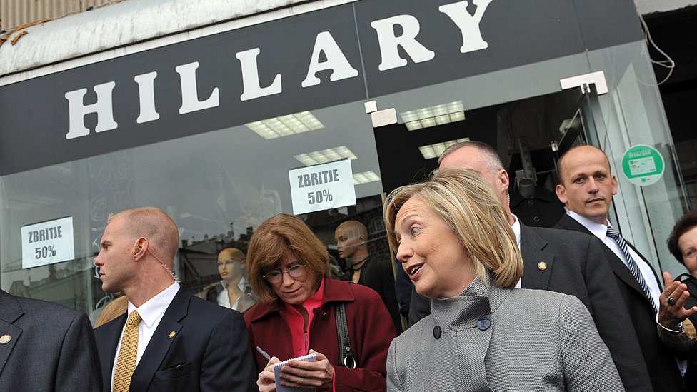 Затем госсекретарь Хиллари Клинтон (C) улыбается, выходя из магазина, названного в ее честь, в Приштине 13 октября 2010 г.