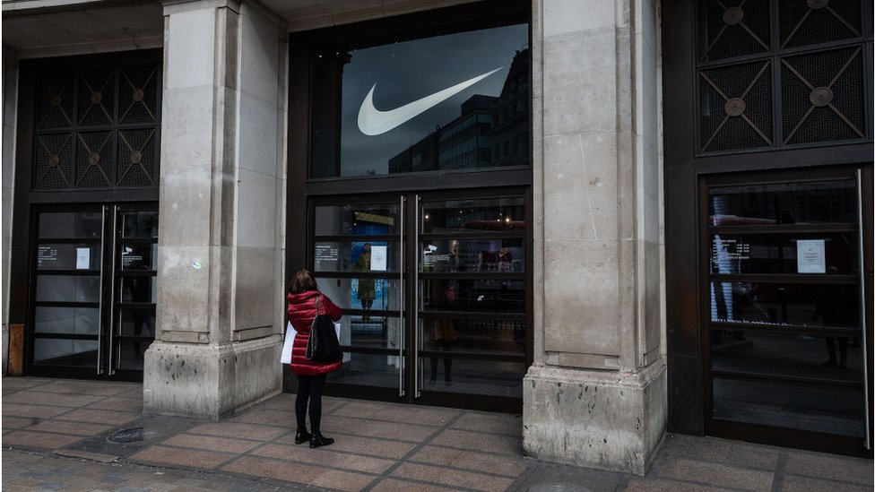 Женщина читает вывеску на двери закрытого магазина Niketown на Оксфорд-стрит в Лондоне.