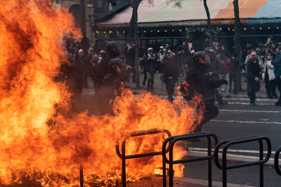 BRAV-M (Brigade de Repression de l'Action Violente - Mobile) riot police officers run behind a burning barricade on March 23, 2023 in Paris