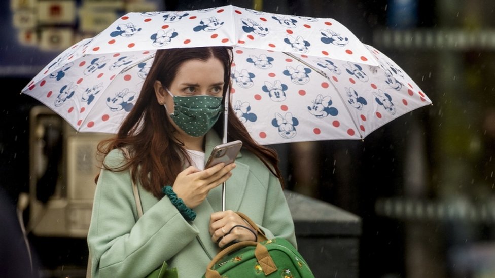 Женщина идет в центре Белфаста под зонтиком в маске для лица