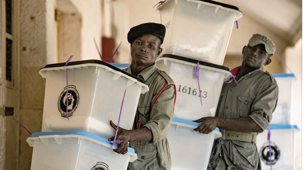 Сотрудники службы безопасности несут урны для голосования на избирательном участке в Дар-эс-Саламе 26 октября 2015 года.