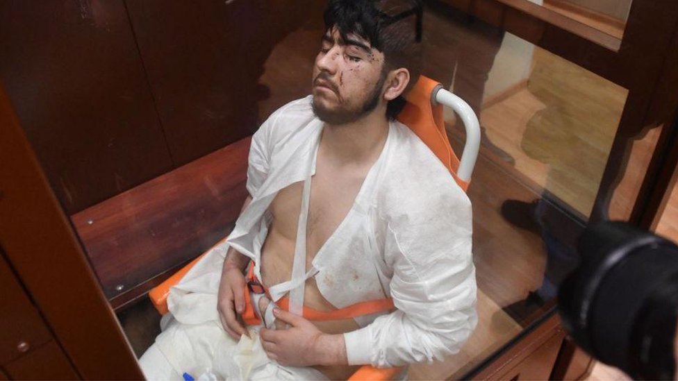 2024年3月25日，穆罕默德索比爾·法伊佐夫在莫斯科法庭上。他身著白色醫院服裝，腰部敞開，閉著眼睛，腿上放著導管引流袋。