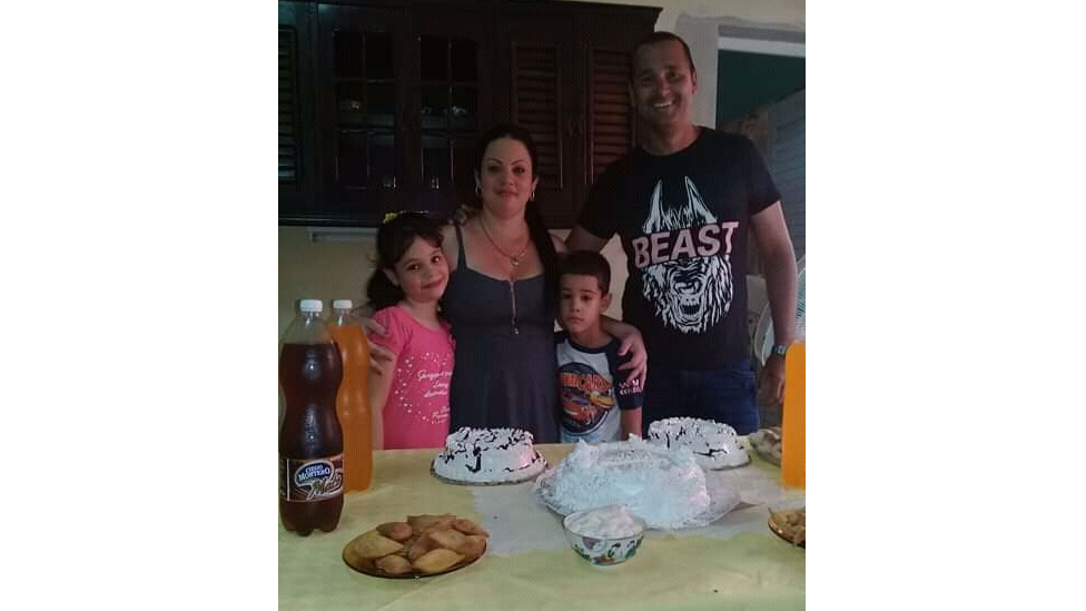 O casal e os dois filhos posam para foto em frente a mesa de aniversário