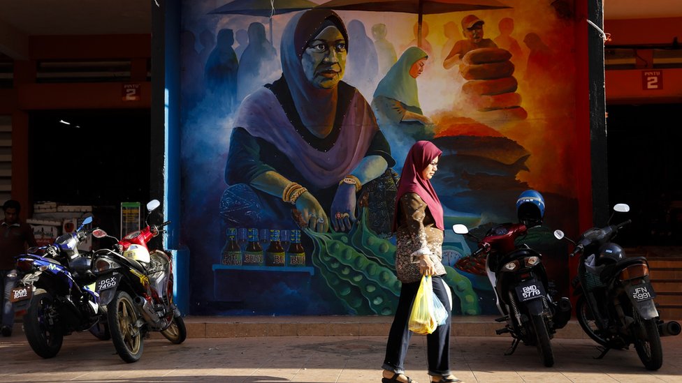 A woman walks past a mural at the central Siti Khadijah market