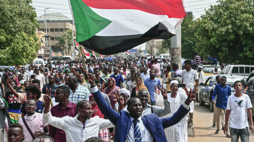 Мужчина демонстрирует знак победы, размахивая суданским национальным флагом во время массовой демонстрации