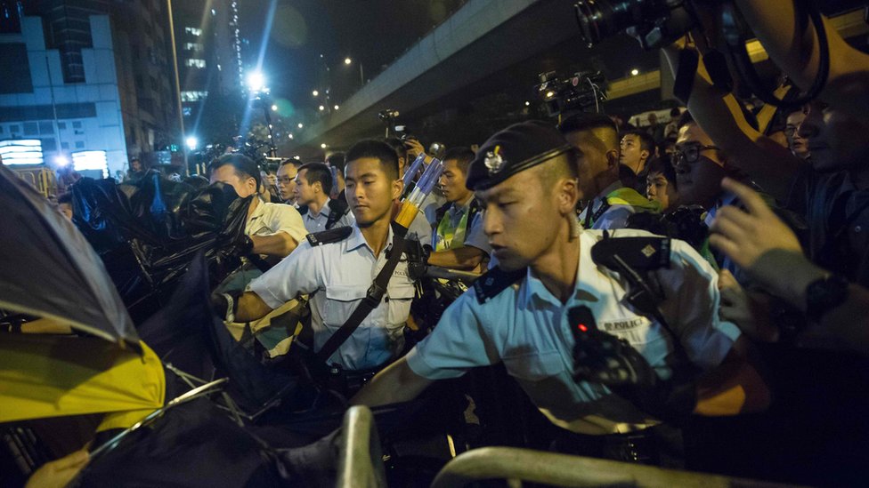 Полиция использовала перцовый баллончик, чтобы остановить протестующих у здания китайского офиса Лиасона в Гонконге 6 ноября 2016 года во время акции протеста против ожидаемого толкования конституции города - Основного закона - Постоянным комитетом Национального народного конгресса Китая (NPCSC). попытки признания клятвы недействительными новоизбранными депутатами Баджо Леунгом и Яу Вай-чином в Законодательном совете в прошлом месяце.
