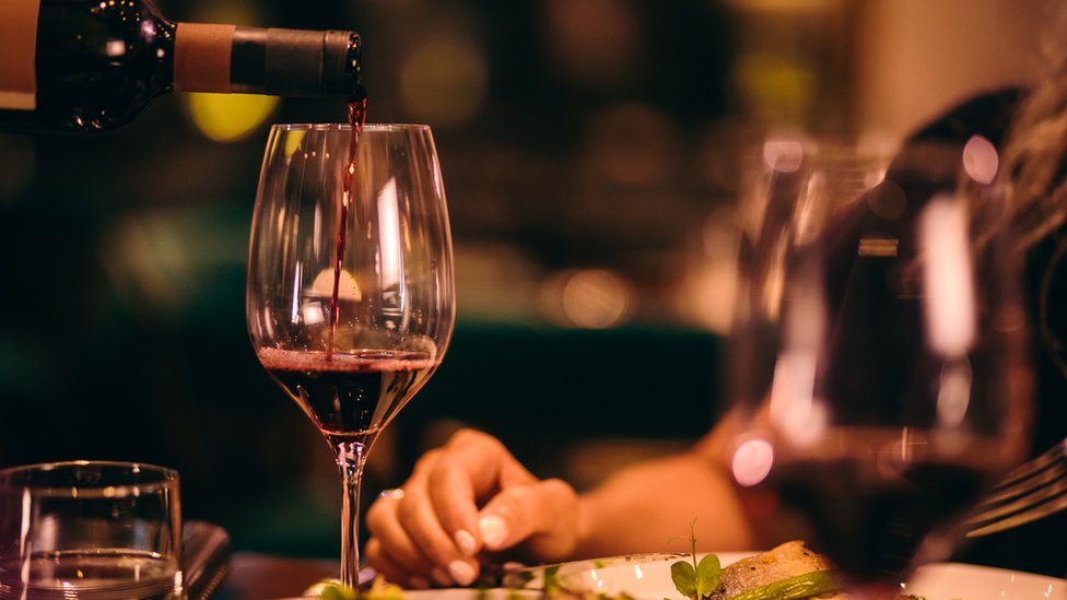 Красное вино наливают в бокал за обеденным столом