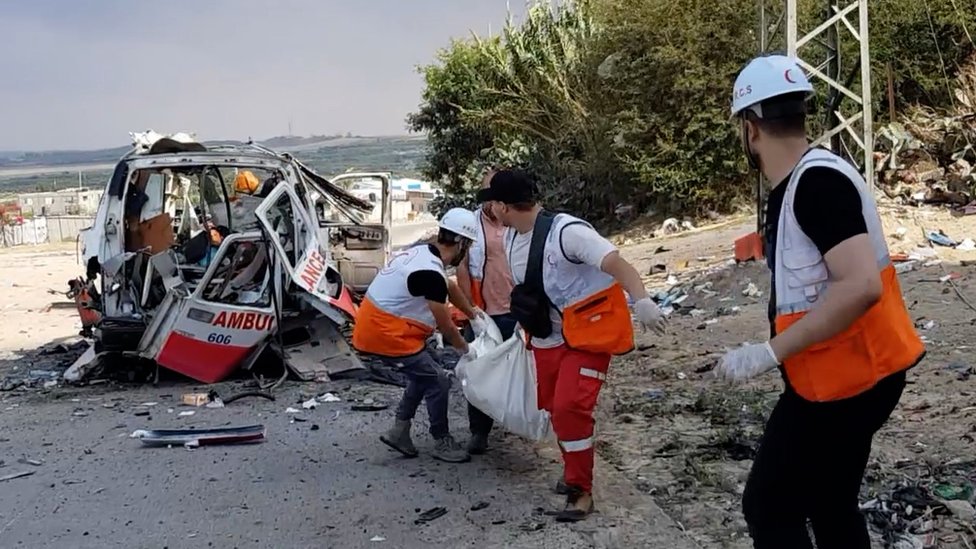 Paramedics carry a body bag from a destroyed ambulance, 11 October