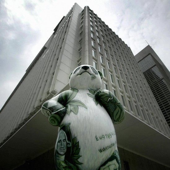 A statue of a panda painted with bamboo leaves and dollar bills outside an office building