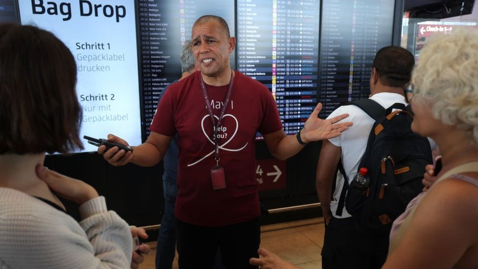 Airport employee Derek Bangura speaks to anxious travellers at BER Berlin Airport during an IT outage that has disrupted airline services worldwide on July 19, 2024 in Schoenefeld, Germany.