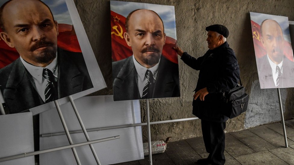 A man examines three colour portraits of Vladimir Lenin