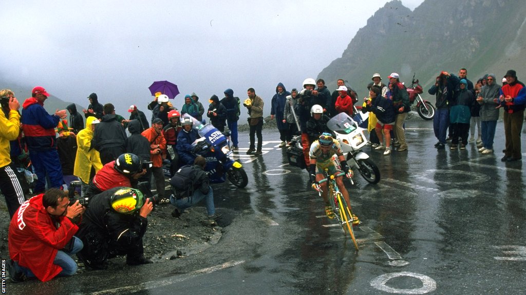 Marco Pantani comes around a hairpin bend with photographers around him and a motorbike behind him