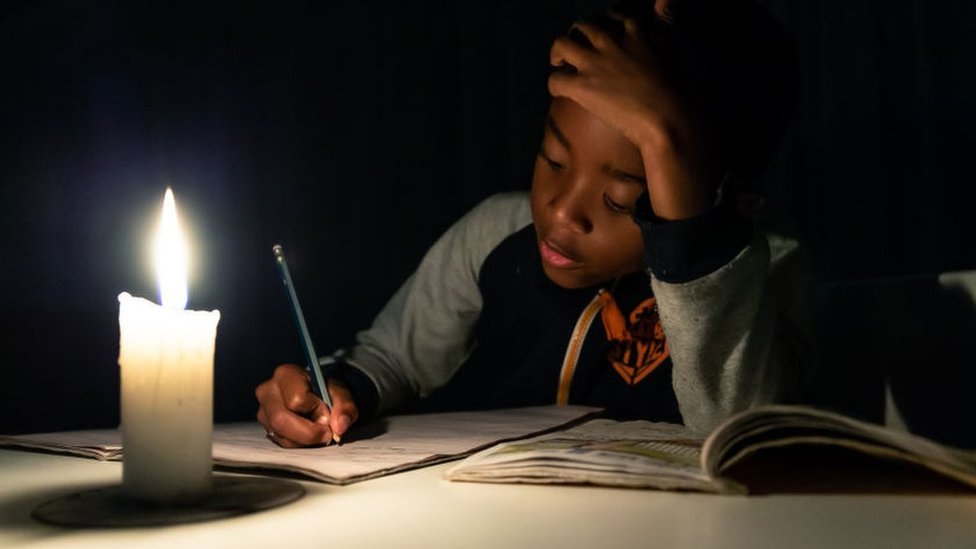 Ребенок делает домашнее задание при свечах в Хараре, Зимбабве - июнь 2019 г.