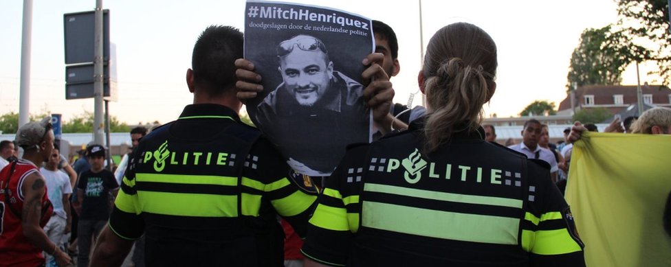 Протестующий держит плакат с изображением погибшего в июне 2015 года уроженца Арубы Митча Энрикеса