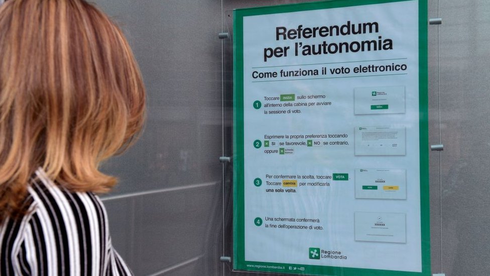 Los resultados de los referendos del domingo no son vinculantes. Una mujer observa un letrero sobre el referendo por la autonomía.