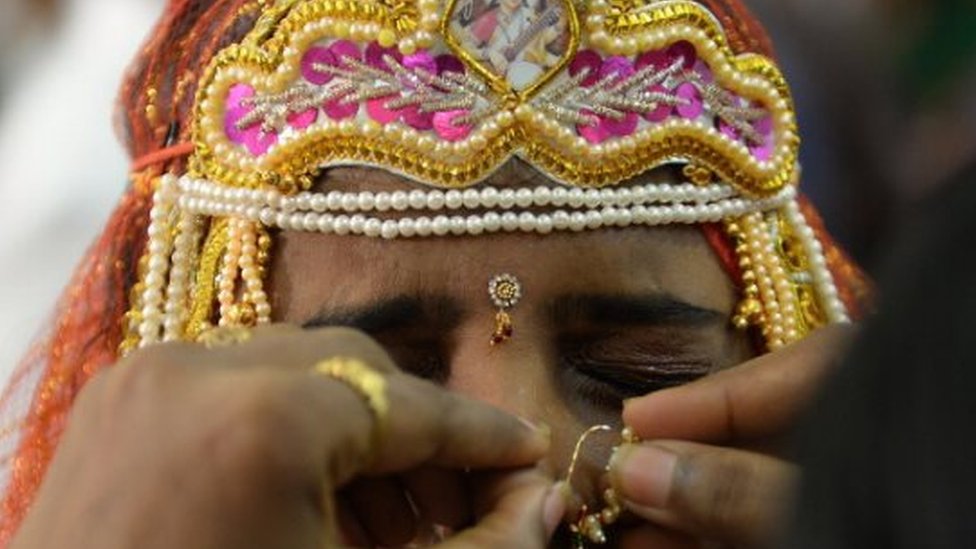 Индийская невеста гримасничает, когда родственница поправляет ей кольцо в носу во время многоконфессиональной массовой свадьбы в Мумбаи 22 июня 2014 года.
