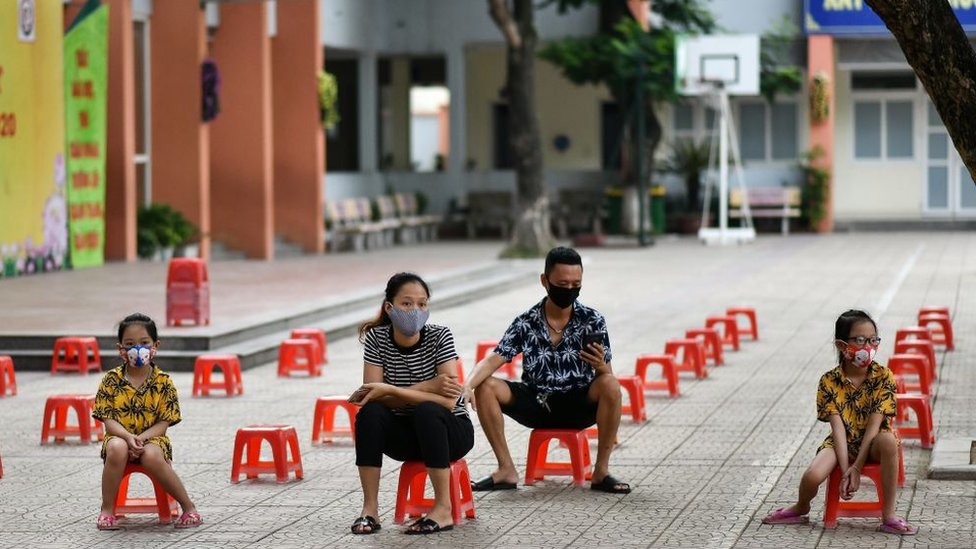 Семья сидит на пластиковых стульях, ожидая тестирования во временном центре быстрого тестирования, поскольку 31 июля 2020 года во Вьетнаме зафиксирован рост случаев коронавируса COVID-19 в Ханое.