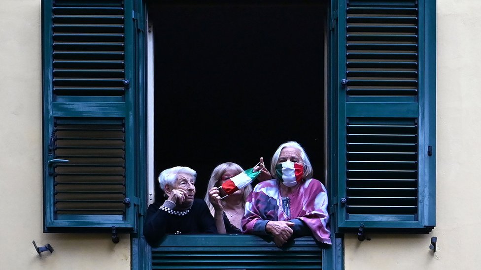 People with protective masks look from their windows at artists performing in the courtyard of a popular apartment building in Rome