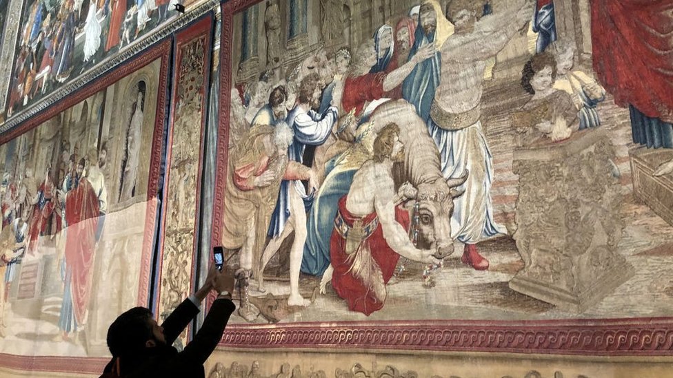 Un hombre toma una imagen del tapiz "El sacrificio de Listra" de Rafael.