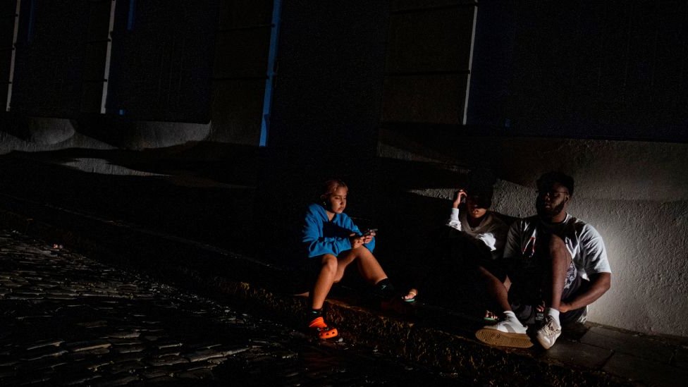 Pessoas em uma calçada em San Juan em uma noite sem serviço elétrico
