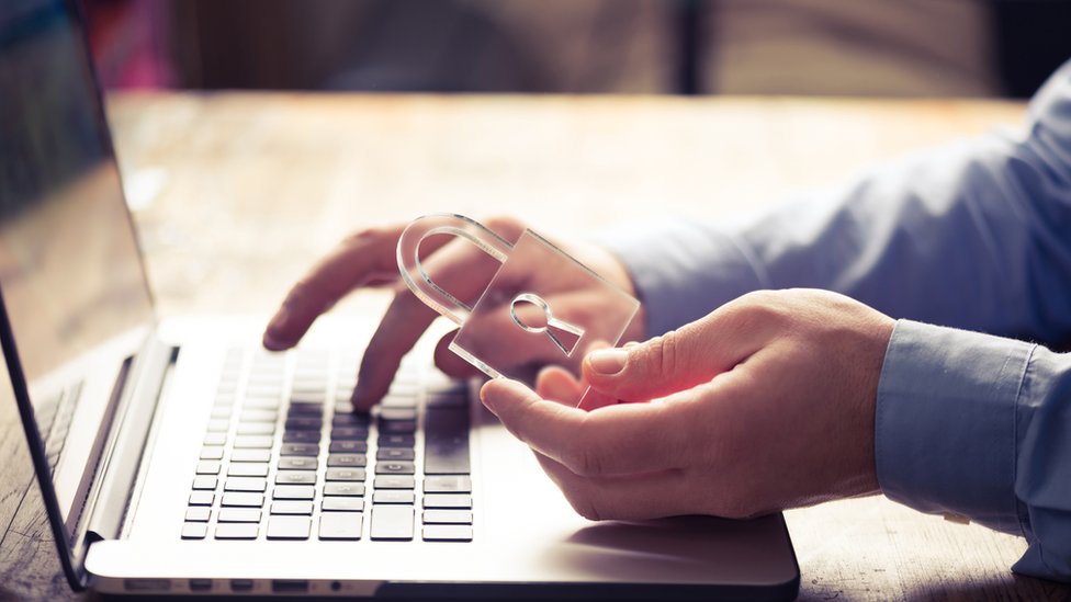 Tu seguridad en internet dependerá de la cantidad de información que compartes y cómo la proteges. Plano de las manos de un hombre frente a su computadora y un candado.